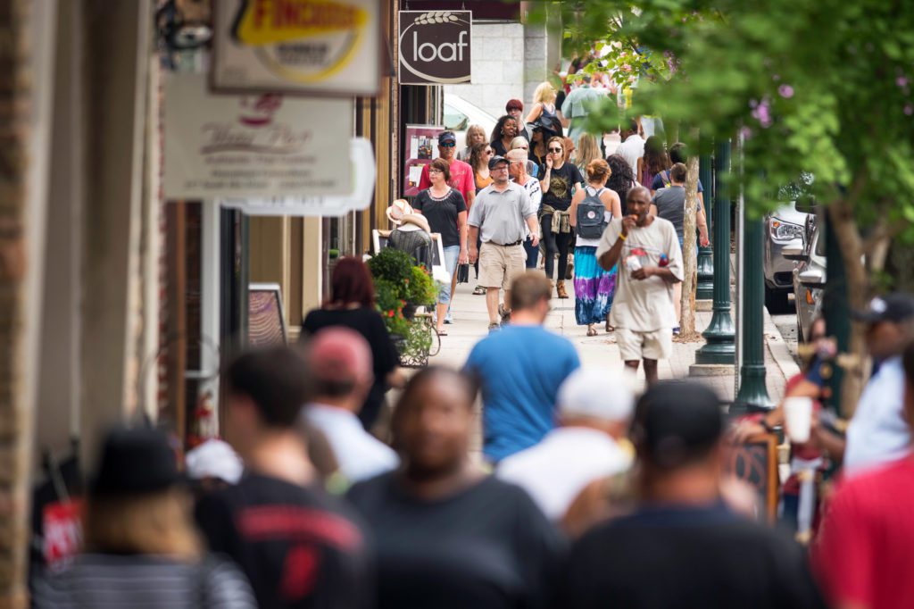 Crowds walking along a busy sidewalk in downtown Greensboro, NC